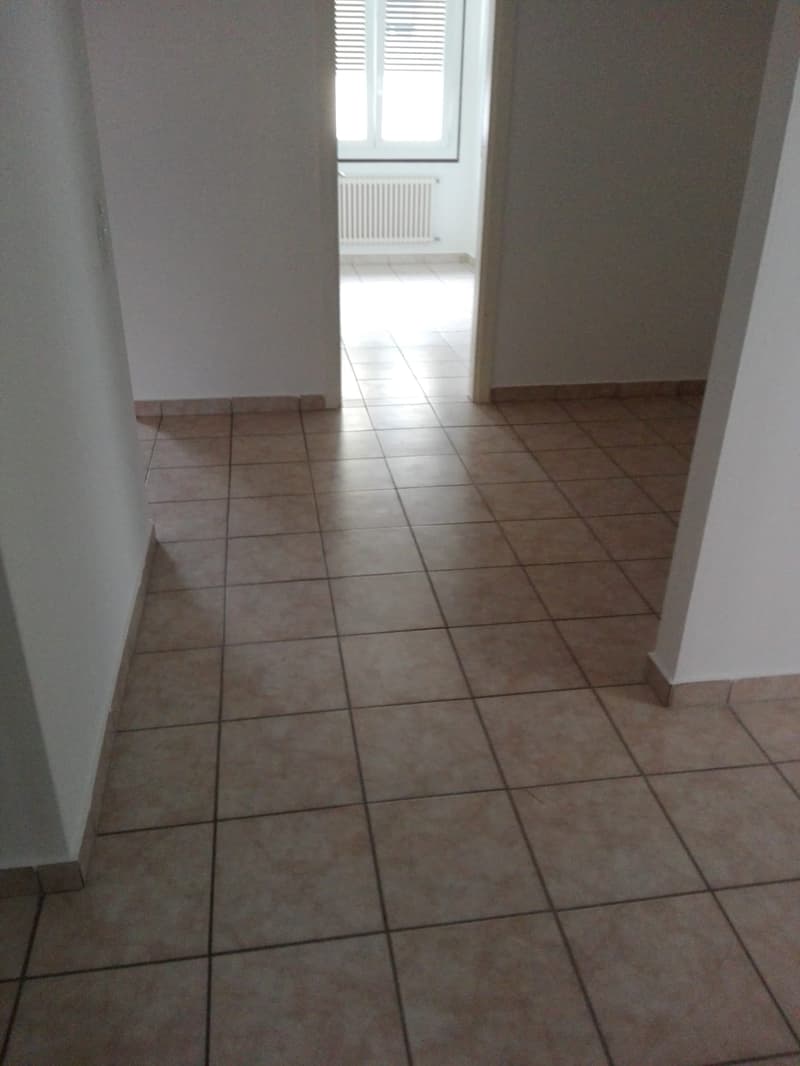 Empty room with white walls, tiled floor, and a window with white shutters.