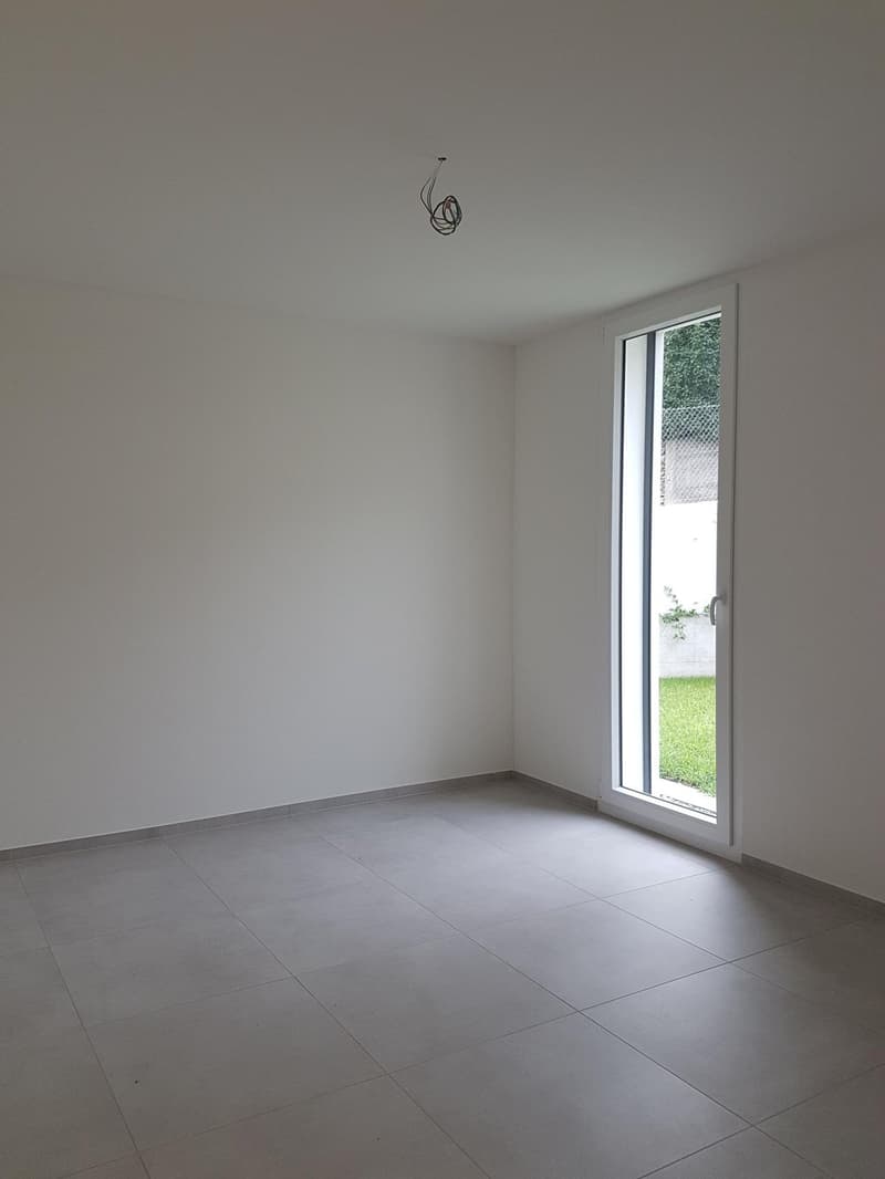 Empty room with tile flooring, white walls, large glass door leading to a grassy area.