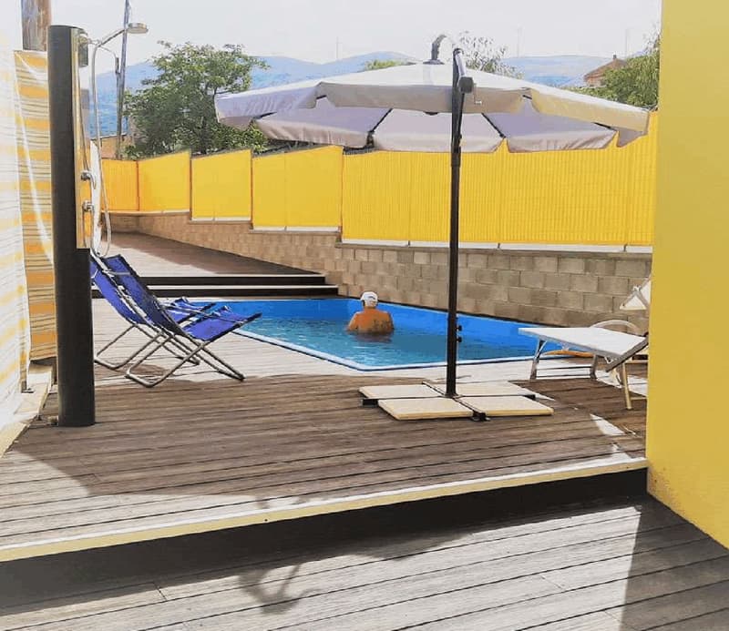 small rectangular pool, pool deck with sun loungers, patio umbrella, yellow fence