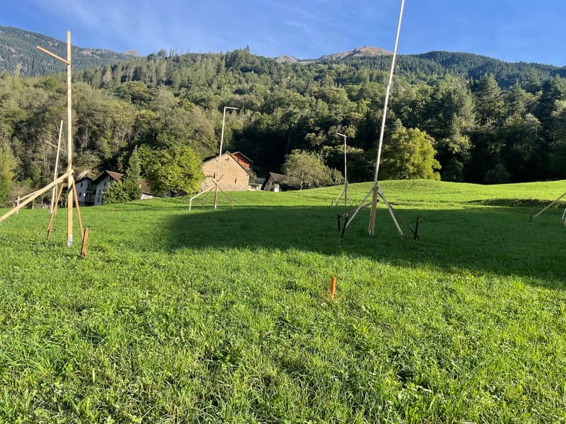 open green field with poles, mountains in the background, houses in the distance