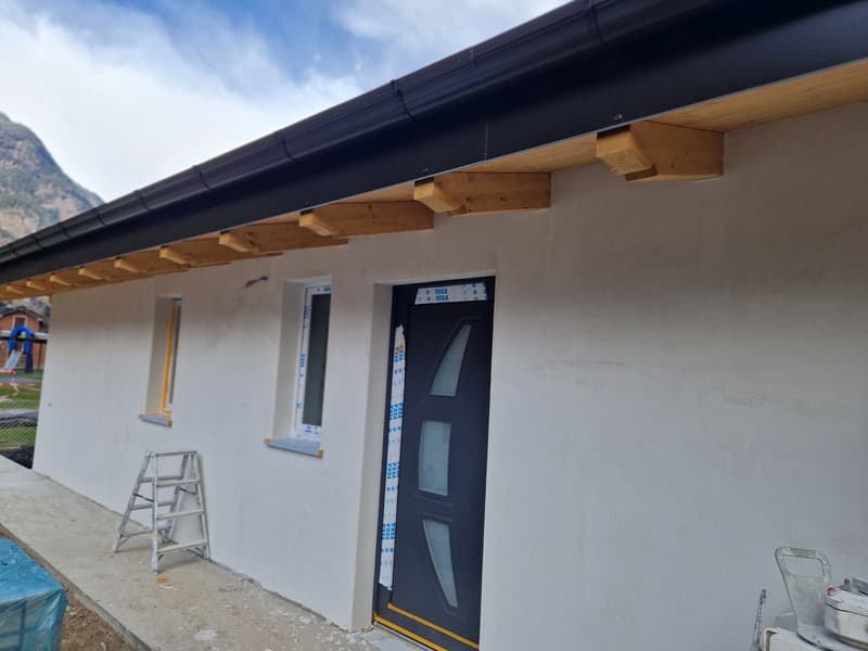 Exterior of a house under construction, white walls, black roof, wooden beams, entrance door, windows, ladder