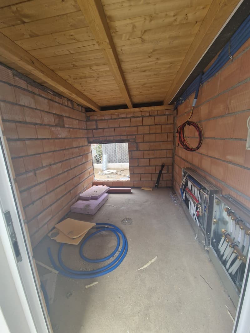 empty room, brick walls, wooden ceiling, small window, electrical box, blue hose