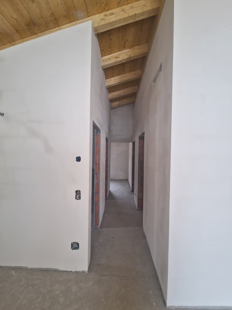 Empty room with white walls, wooden ceiling, concrete floor, brick walls on the side, and doors.