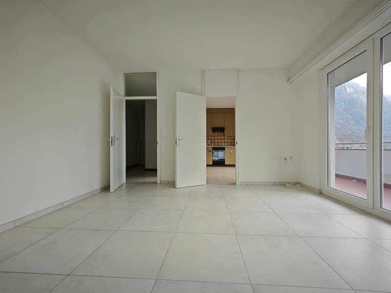 Empty room with tiled floor, open doors leading to other rooms, large windows with balcony access
