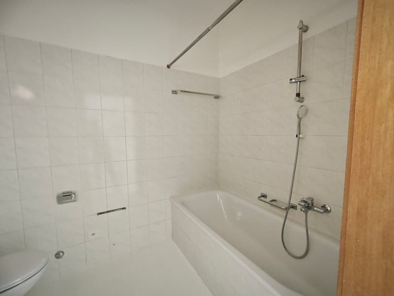 white tiled walls, white bathtub, shower head, toilet, wooden door