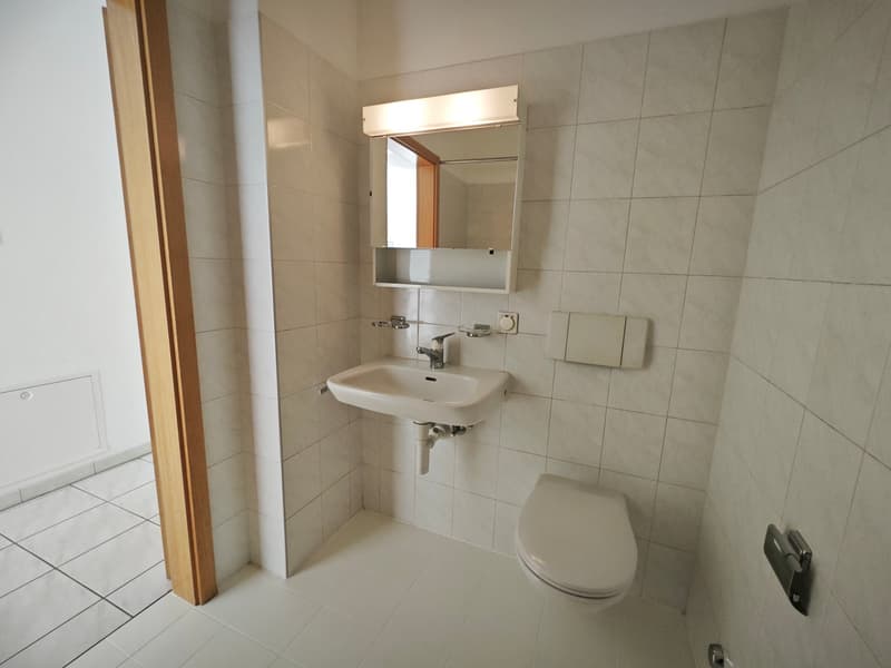 small bathroom with white tiles, sink, mirror, toilet, and a light above the mirror