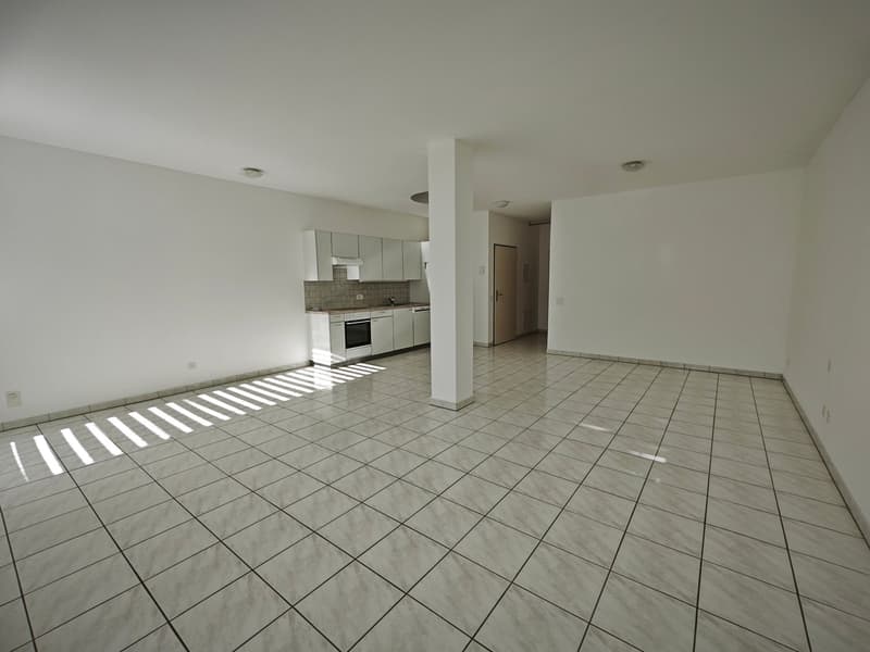 Empty room with white tiled floor, white walls, kitchen with appliances, and a central column.