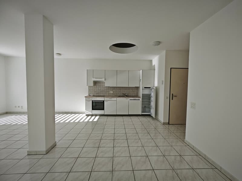 Empty kitchen with white tiles, white cabinets, and a refrigerator.