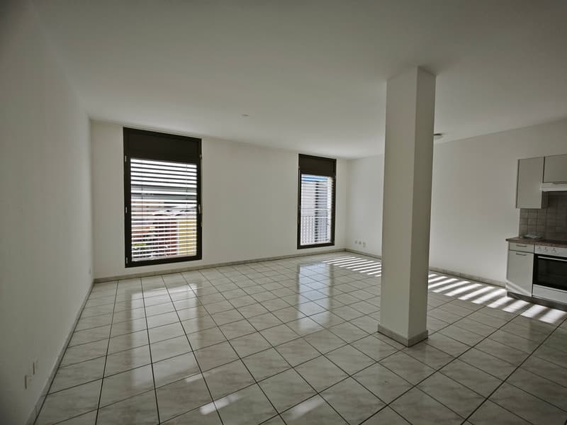 Empty room, white walls, tiled floor, two windows with balcony, kitchen area with oven