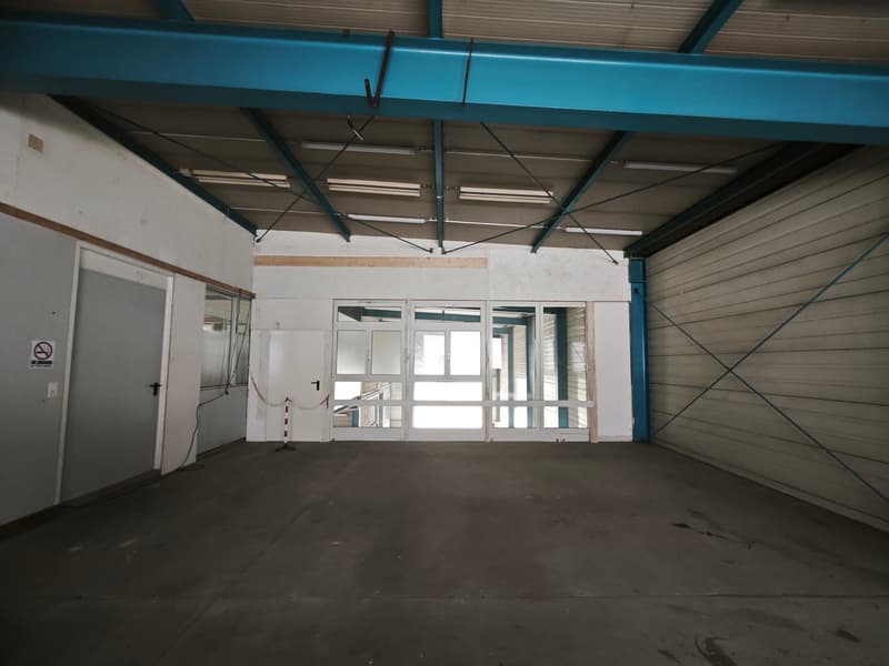 Empty warehouse with concrete floor, metal beams, and large glass doors.
