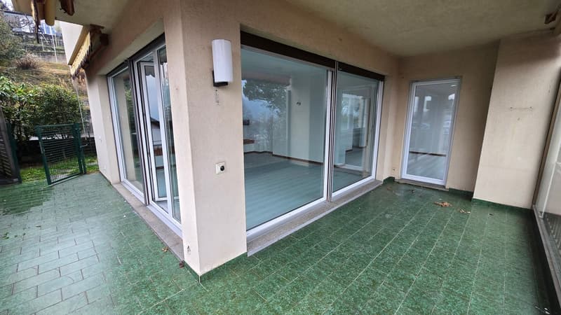 The terrace has green tile flooring and is surrounded by large glass sliding doors.