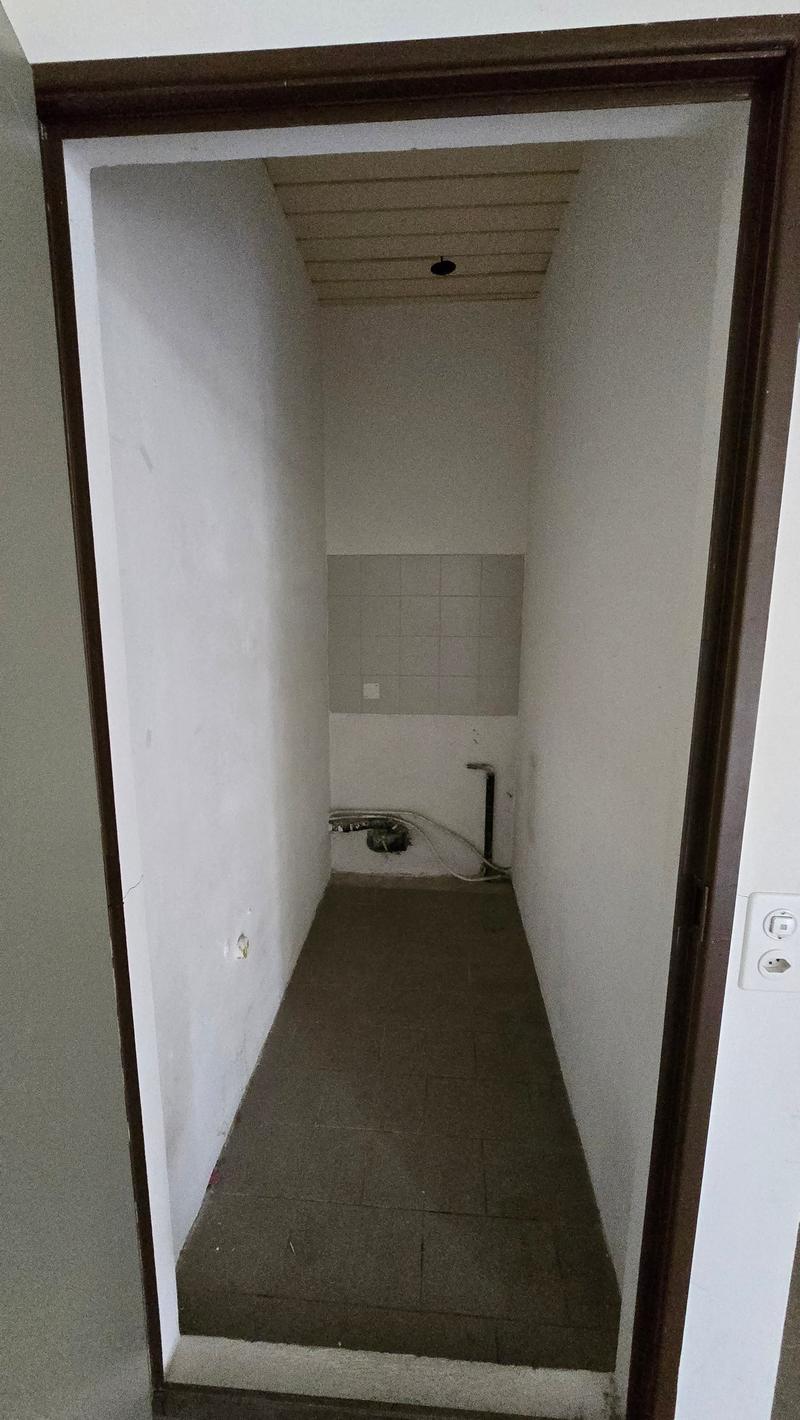 An empty room with bare walls, a tiled section, and a carpeted floor. There are electrical outlets and a power outlet on the wall.