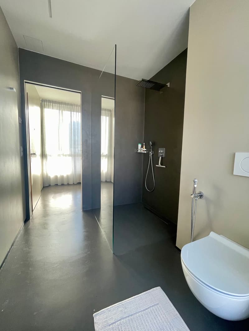 Bathroom with glass shower, floor and wall tiles, toilet, sink, window with curtains