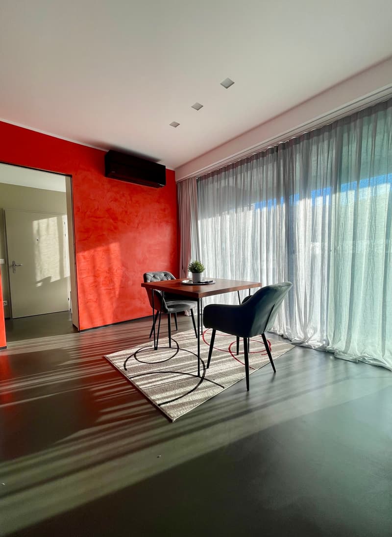 Dining area with red wall, large window, wooden table, black chairs, carpet, potted plant