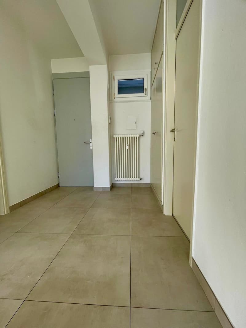 Empty room with tiled floor, radiator, small window above radiator, glass door on the left side, and two doors on the right.
