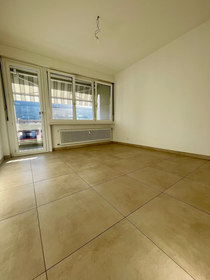 empty room with tiled flooring, white walls, sliding glass doors with blinds, large windows, white radiator