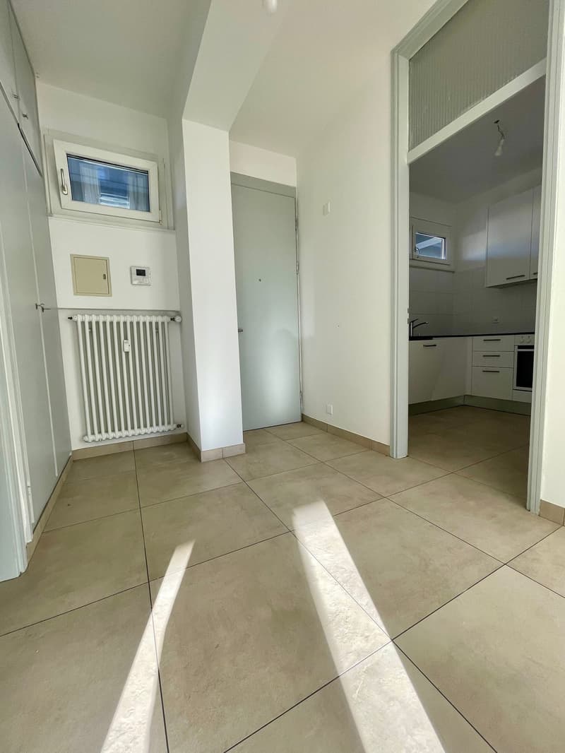 Empty room, modern interior, white walls, beige tile flooring, open door, large window, white radiator