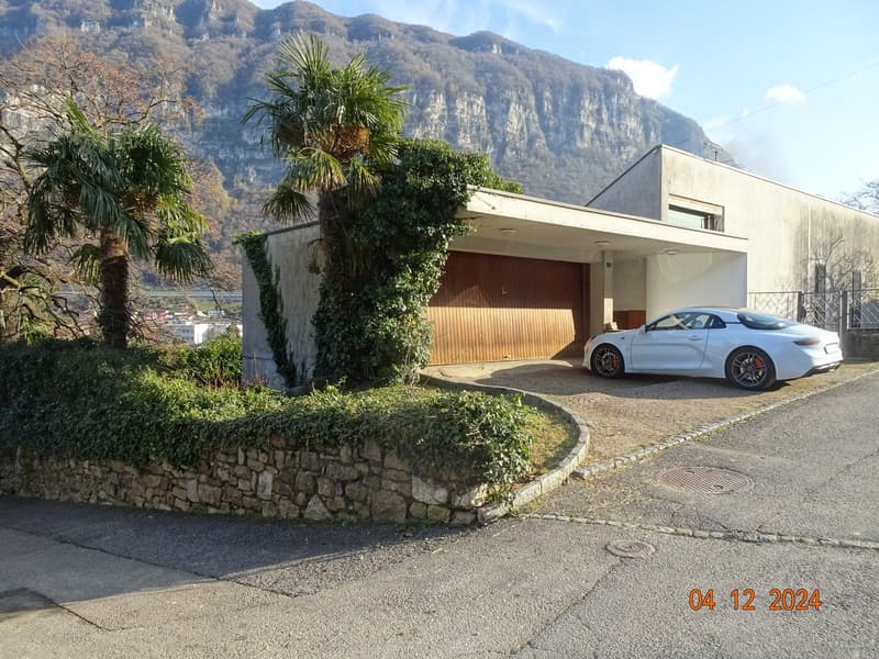 Single story house with wooden garage, stone wall surrounding the property, large windows, scenic mountain view