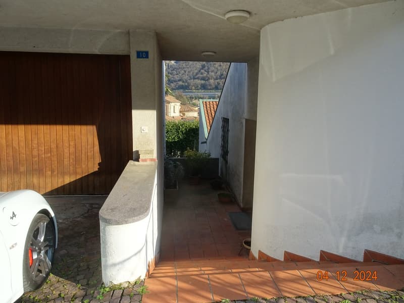 Exterior of a house with entrance steps, brick floors, a wooden door, white walls, plants, and a scenic view in the background.