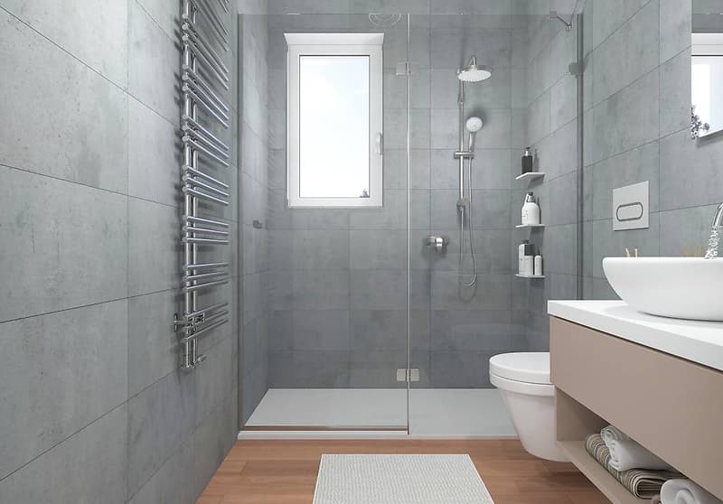 Gray tiled walls, glass walk-in shower, white toilet, white porcelain sink, chrome shower head and towel warmer