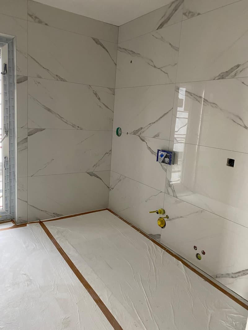 Bathroom with marble tiles, white floor, glass door, unfinished walls