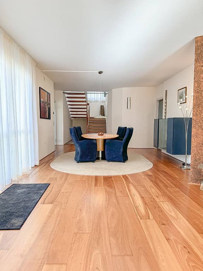 hardwood floor, round dining table with chairs, staircase, art paintings on the wall, curtains, lamps
