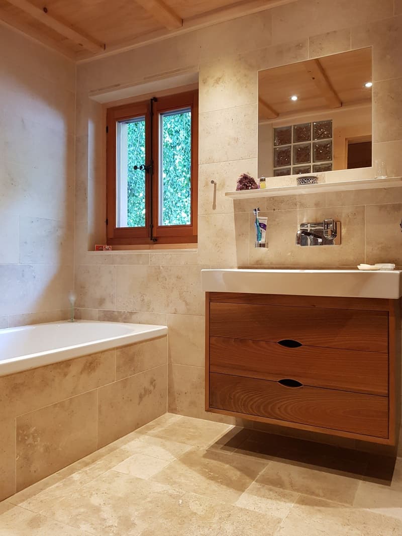 Bathtub, white sink, mirror, wooden cabinet, faucet, window, tiled floor