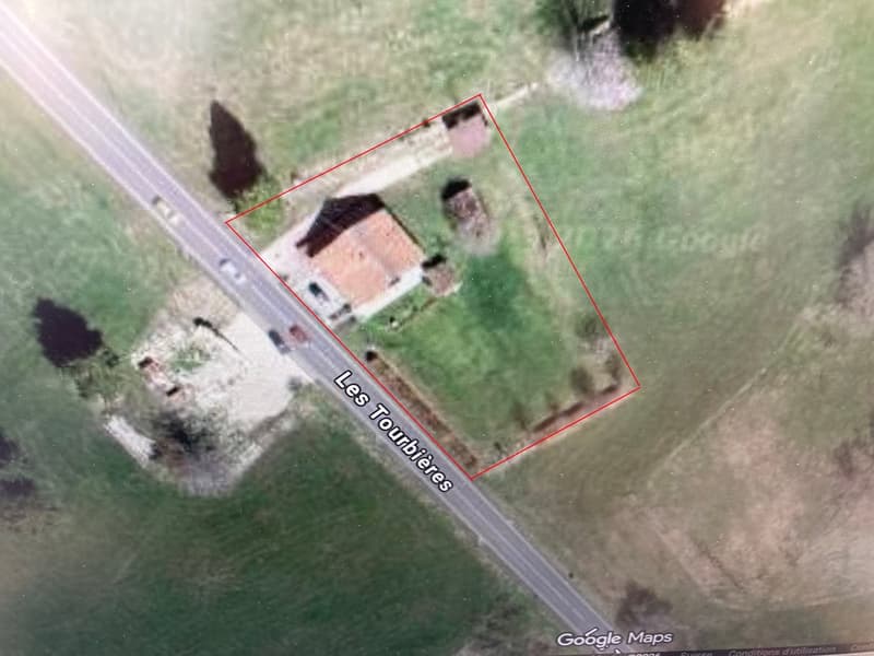 House with a tiled roof, surrounded by a large grassy field, located near a road.