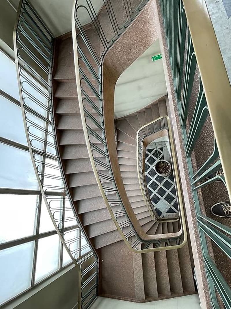 Double flight staircase with golden handrails, beige tiles, glass windows, tiled landing area