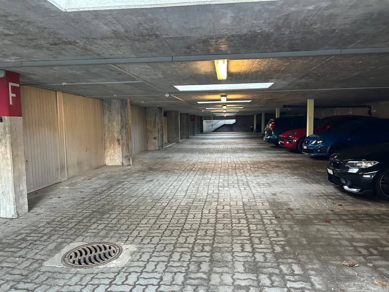 brick floor, white ceiling, four cars parked, one on the left, three on the right, yellow lighting
