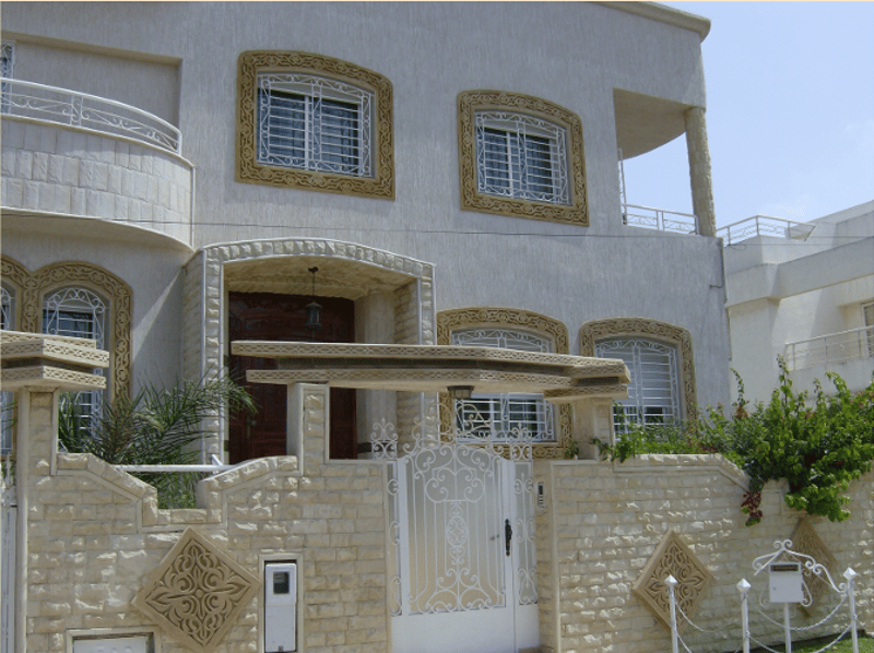 Two-story white house with arched windows, decorative railings, large front gate, garden entrance, decorative brickwork