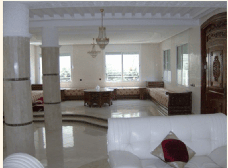 White leather couch with two pillows, marble floor, round wooden table, large arched windows