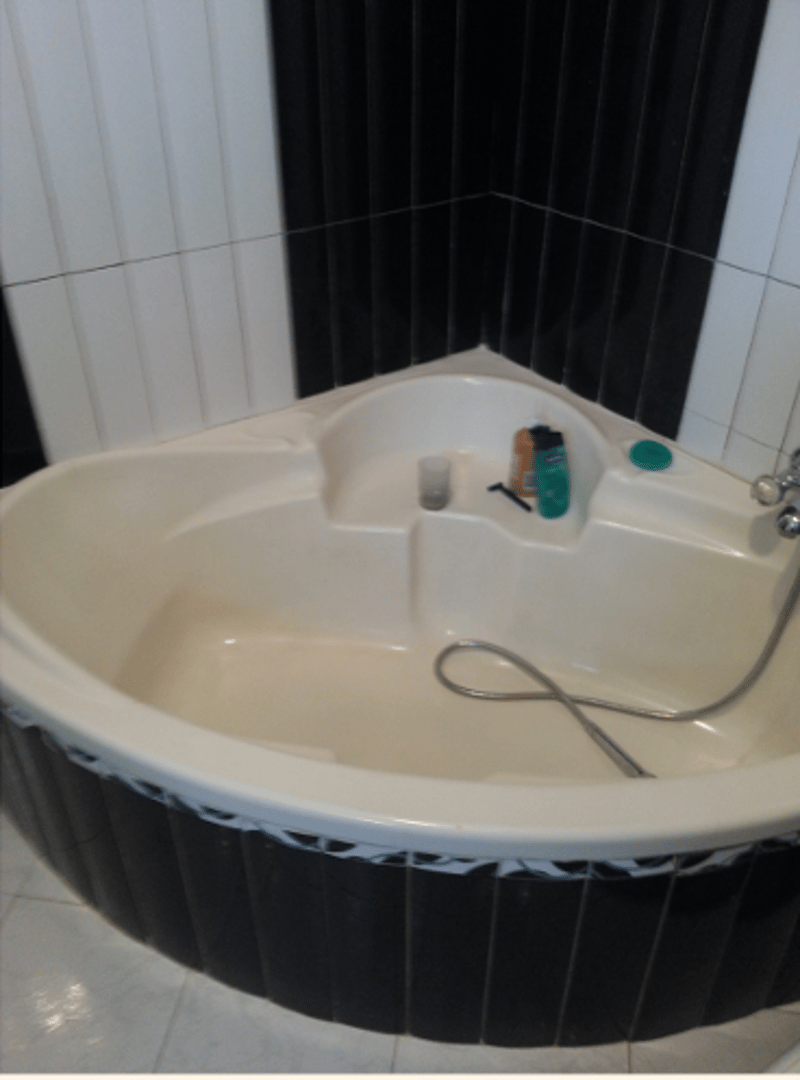 An empty corner bathtub with shelves, attached to tiled walls, and a water faucet on the right.