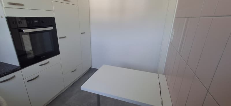 modern kitchen area with integrated oven, white countertops, white cabinets, grey floor, foldable dining table