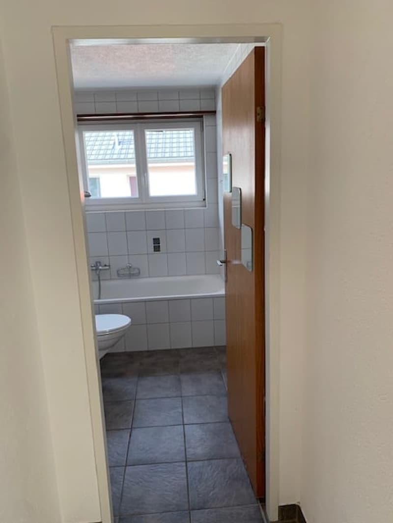 Bathroom: white bathtub, white tiles, white walls, window, toilet, open door