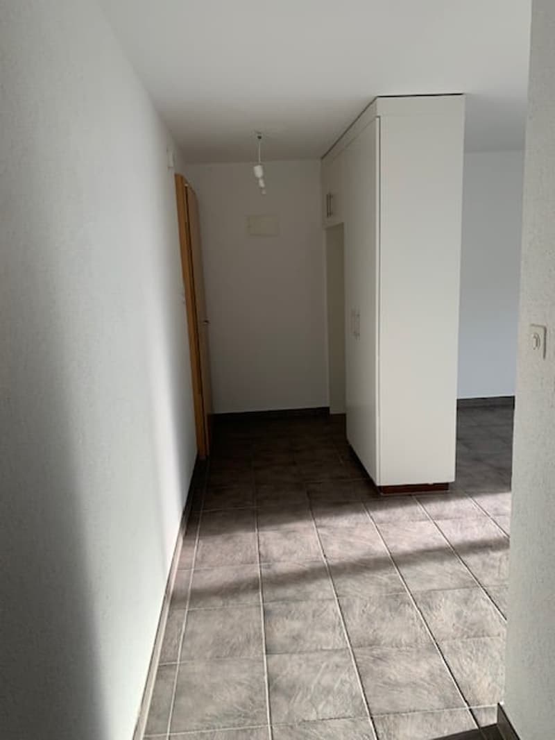 Corridor, white walls, tiled floor, wardrobe on right side, open wooden door