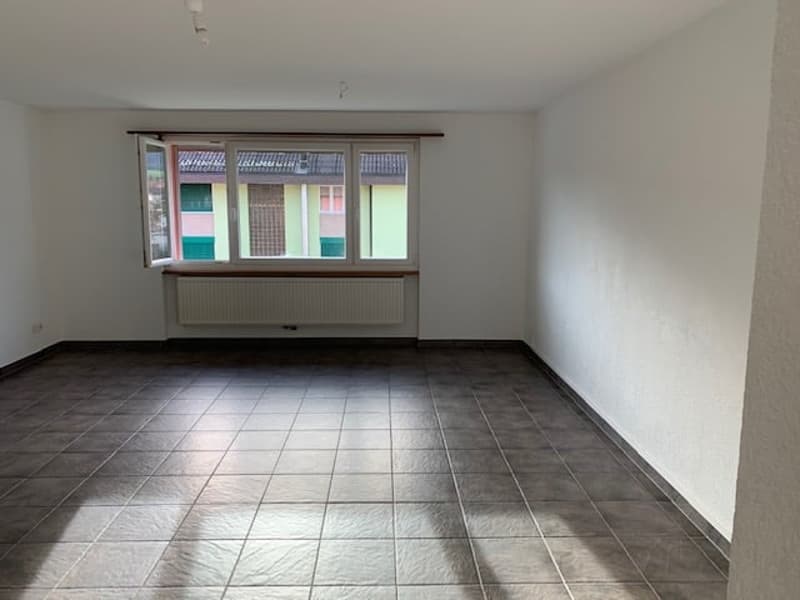 Empty room with white walls, tiled floor, large window, and a radiator below the window.