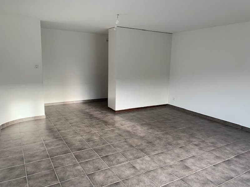 Empty room with white walls and gray tiled floor, small door, open ceiling