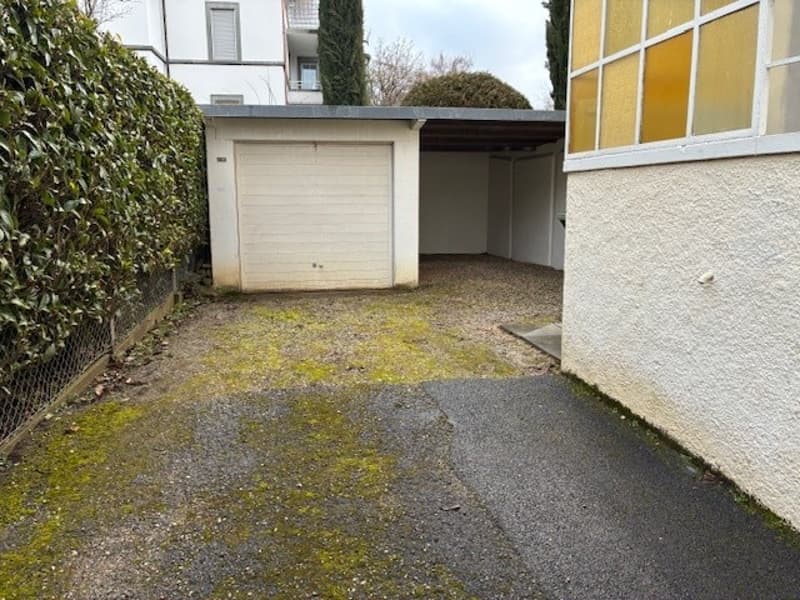An outdoor car parking area with a white garage, next to a building with windows.