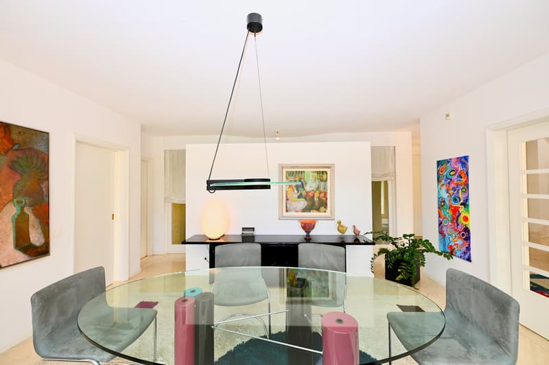 modern dining room with round glass table, upholstered chairs, black console table, glass lamp, artwork on the walls, potted plant