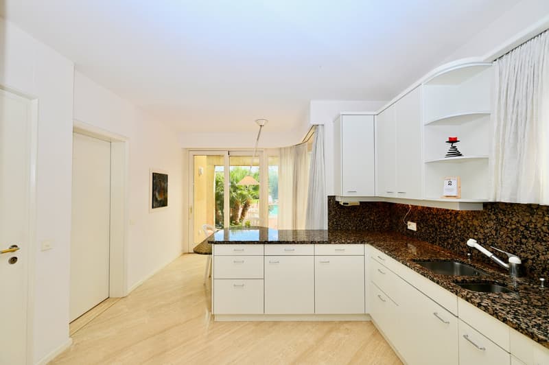 White cabinetry, black granite countertops, stainless steel sink with faucet, kitchen island, white walls, hardwood floors, glass sliding doors leading to the outside, pendant light