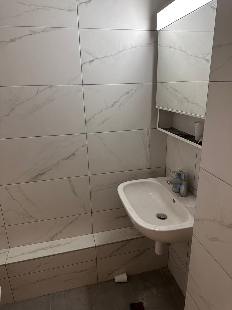 tiled walls, modern shower, white sink, marble countertops, vanity mirror