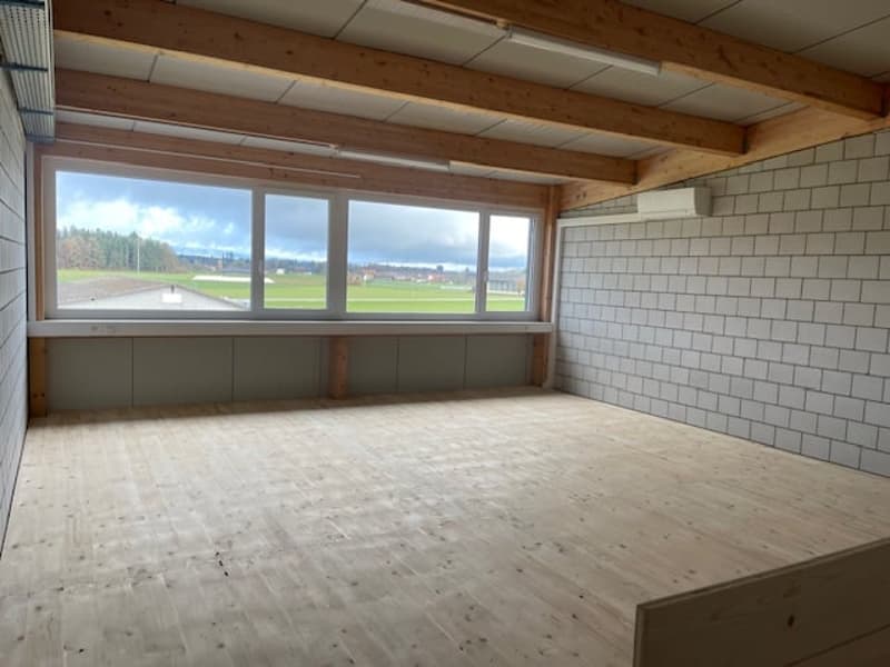 Open room, wooden floor, large windows, white tiles, beam ceiling
