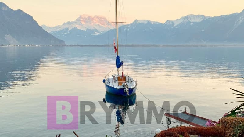 A sailboat is docked on the lake with mountains in the background.