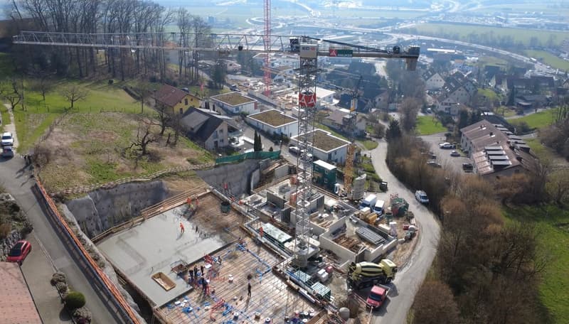 Aerial view of a construction site with multiple buildings under construction, cranes, and vehicles.
