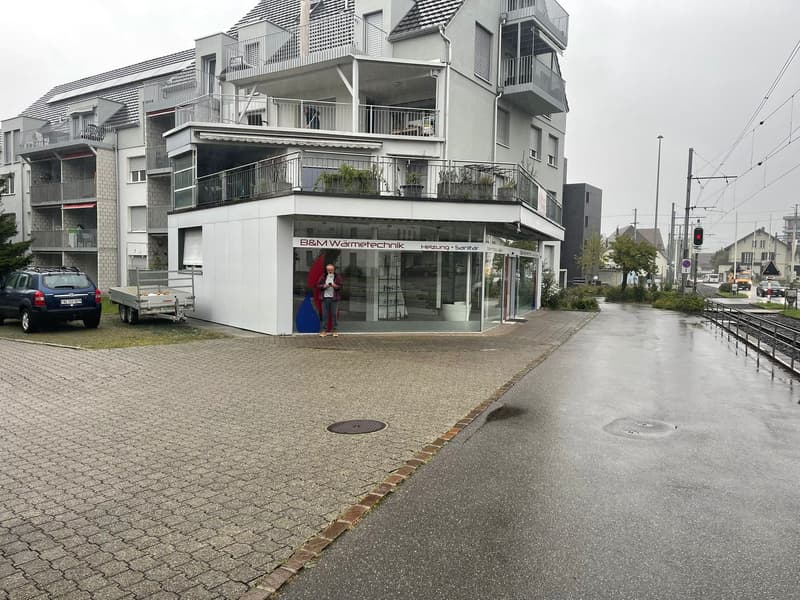 An apartment building with several floors and a storefront at the ground floor, with a car parked in front of it.
