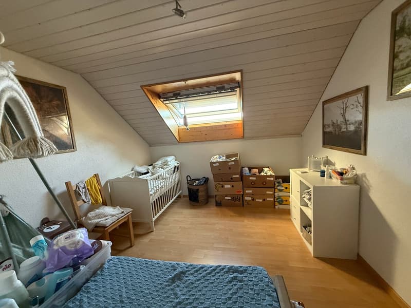 A room with wooden floor, a crib, a chair, a shelf, a storage box, a basket, and a storage box with a lamp