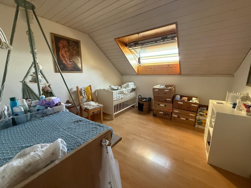 A room with a bed, crib, wooden chair, storage boxes, and a painting on the wall.