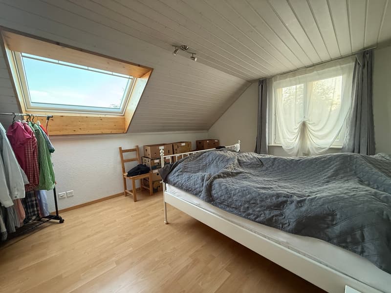 bedroom with wooden floor, bed, chair, boxes, clothes on hangers, skylight, window with curtains