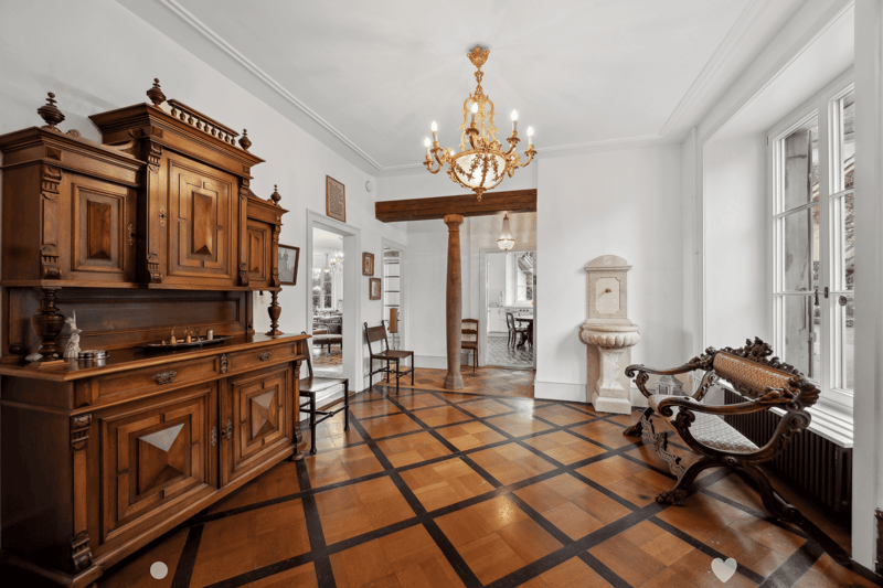 elaborate wooden furniture, hardwood floor with black trim, chandelier, wooden bench, radiator, windows